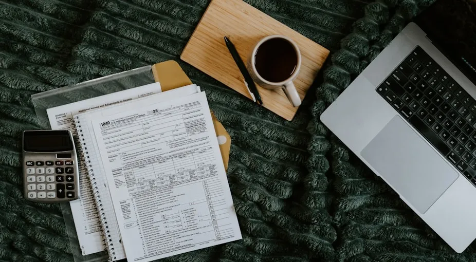 Laptop, papers, calculator, and coffee on blanket.